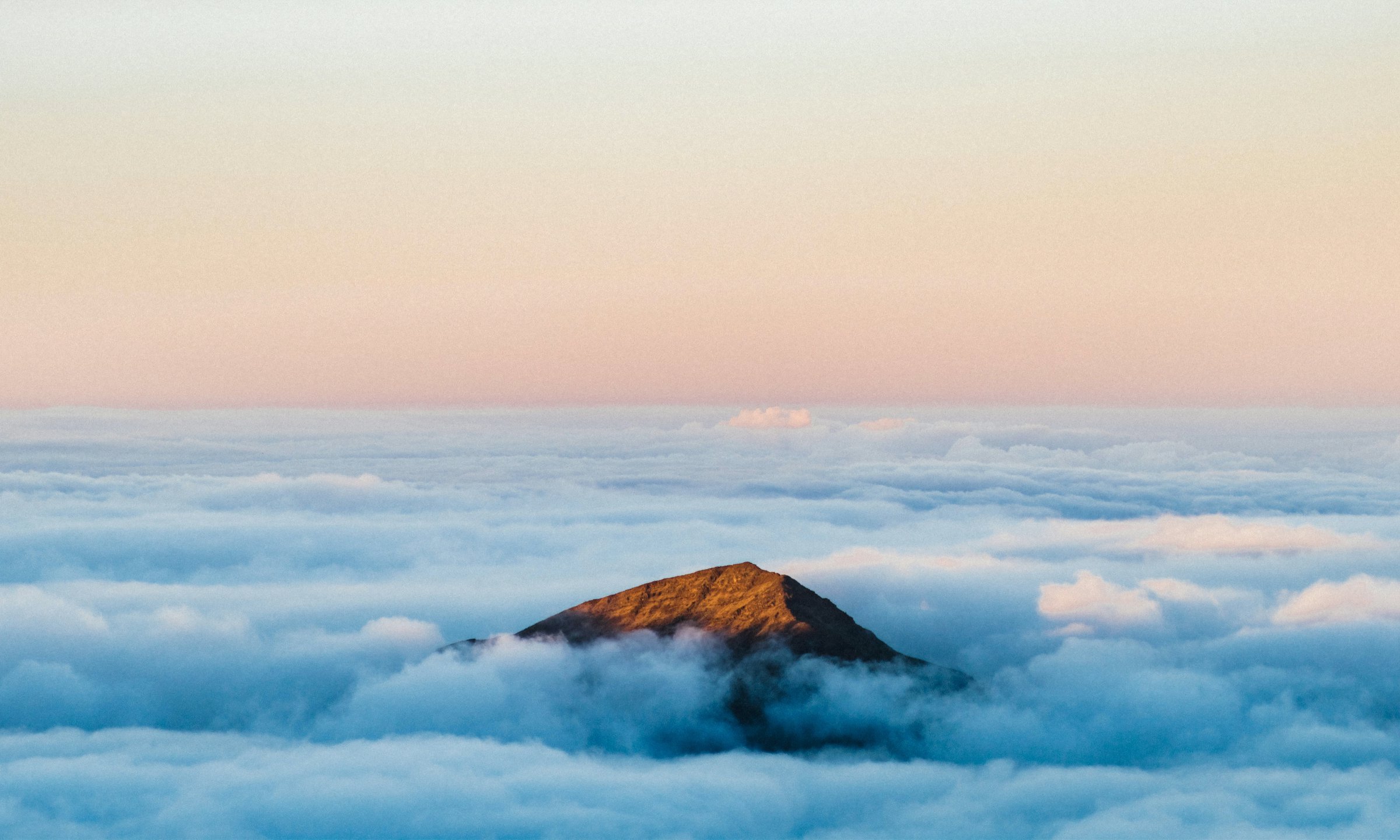 A lone mountain peak rising above a sea of clouds at sunrise